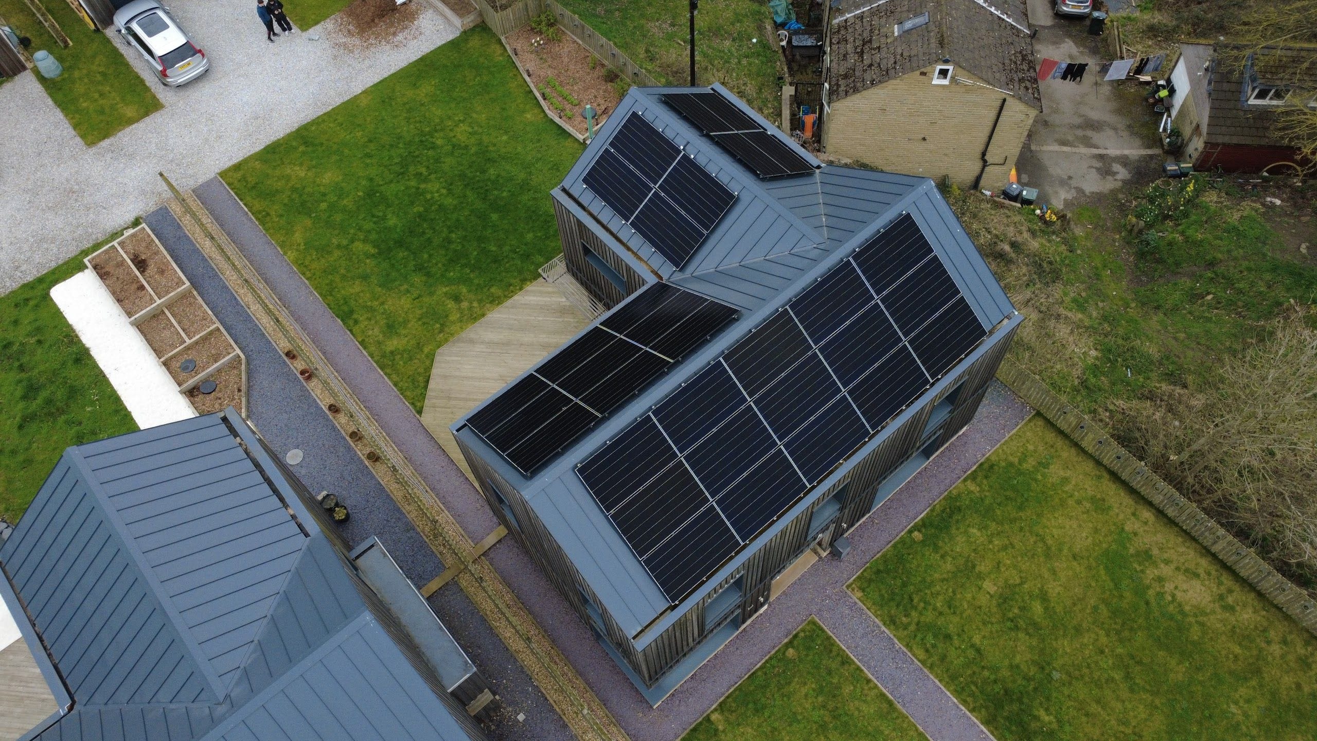 A timber-clad house with arrays on its grey metal roof slopes, seen from a drone above the gardens