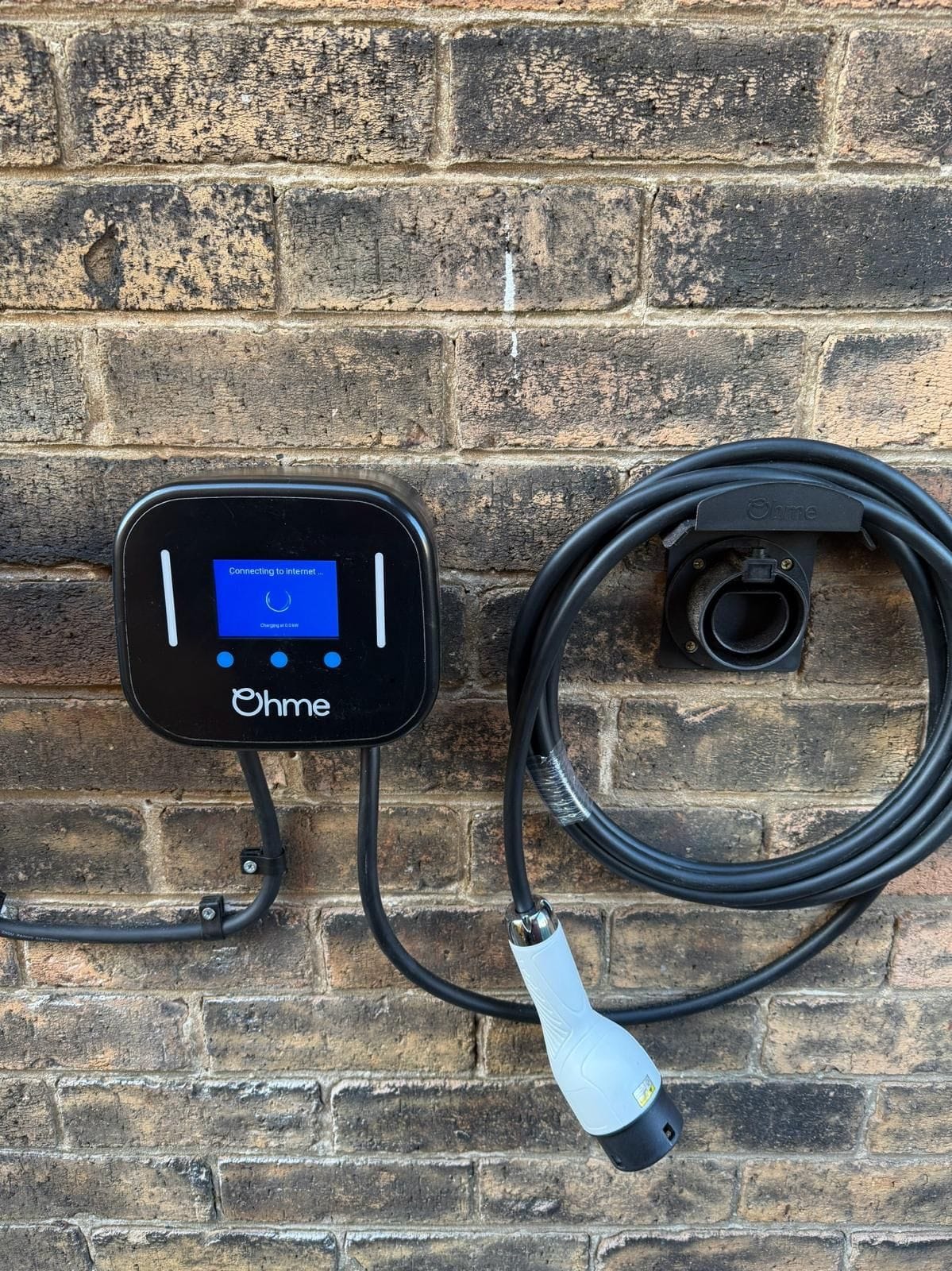 An Ohme car charger on a stone wall