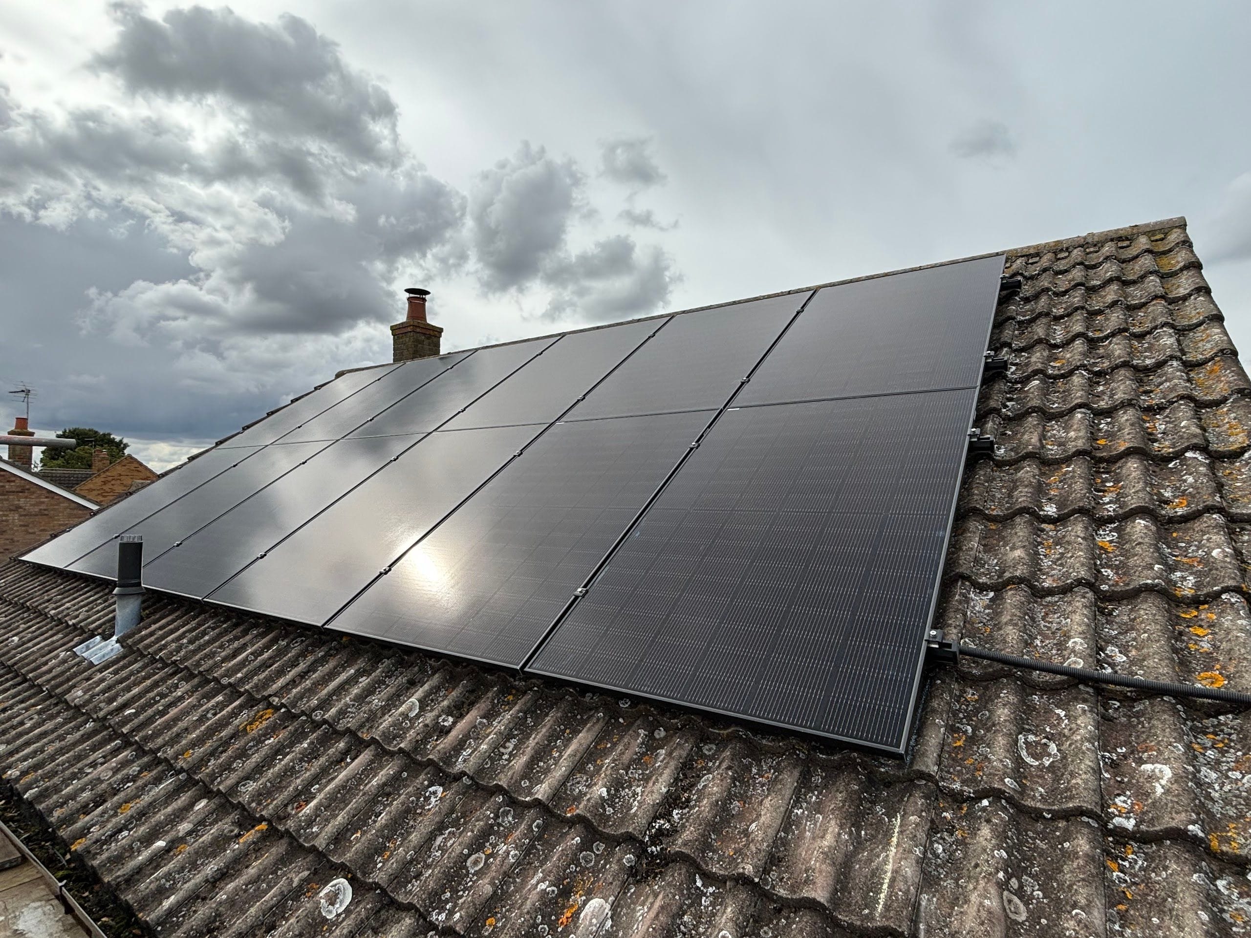 A finished array of black panels on a concrete-tile roof under a cloudy sky