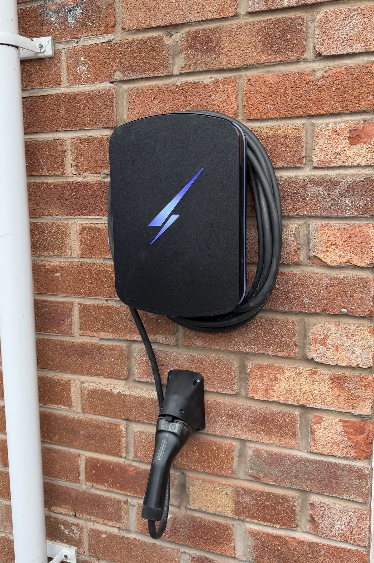 A home car charger on a brick wall, its tethered cable coiled round it