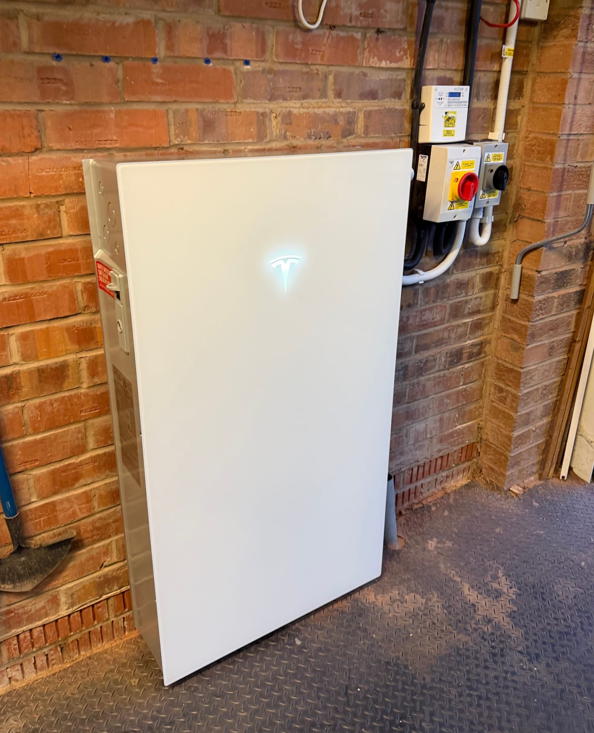 A home battery on a brick wall inside a garage, its isolators on the wall beside it